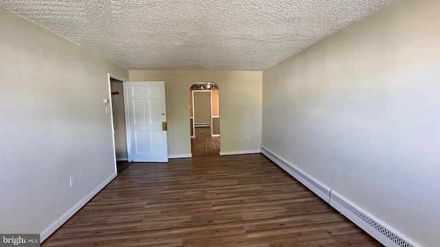 empty room with a textured ceiling, dark hardwood / wood-style floors, and a baseboard heating unit