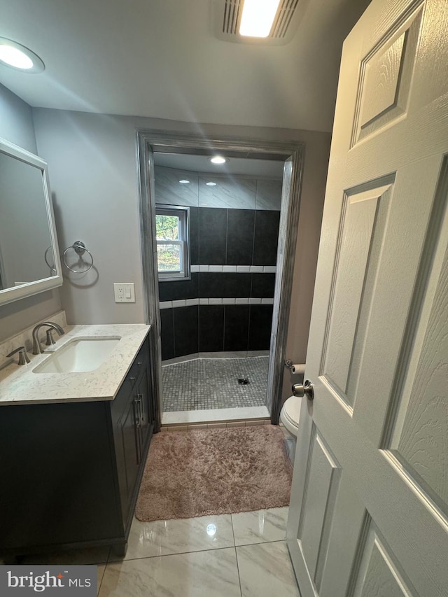 bathroom with toilet, vanity, and tiled shower