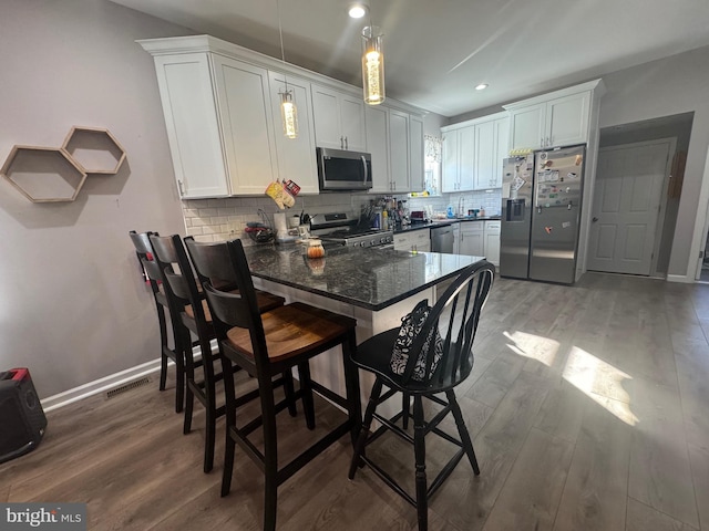 kitchen with kitchen peninsula, tasteful backsplash, stainless steel appliances, hardwood / wood-style flooring, and white cabinetry