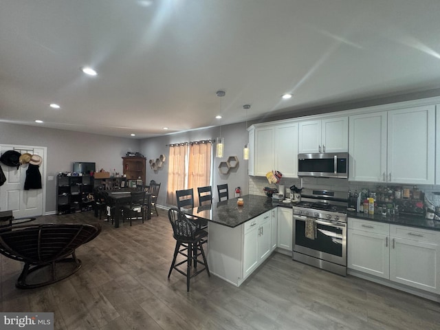 kitchen with white cabinets, hardwood / wood-style flooring, kitchen peninsula, and appliances with stainless steel finishes