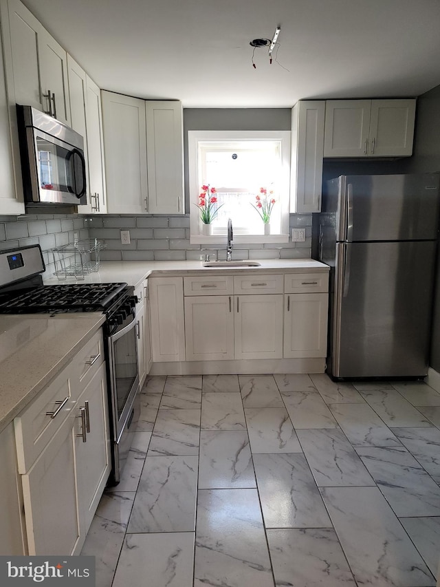 kitchen with tasteful backsplash, sink, white cabinets, and appliances with stainless steel finishes