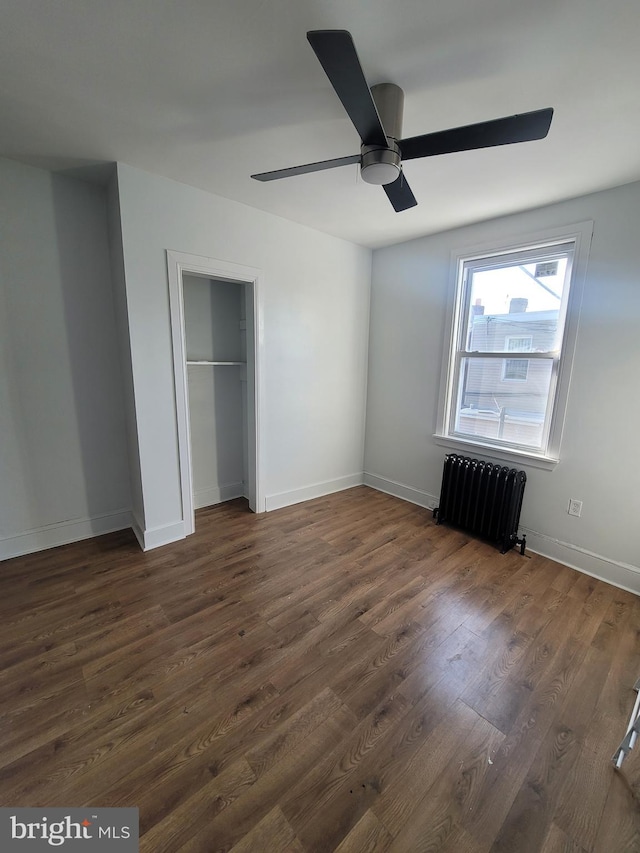 unfurnished bedroom with ceiling fan, dark wood-type flooring, radiator, and a closet