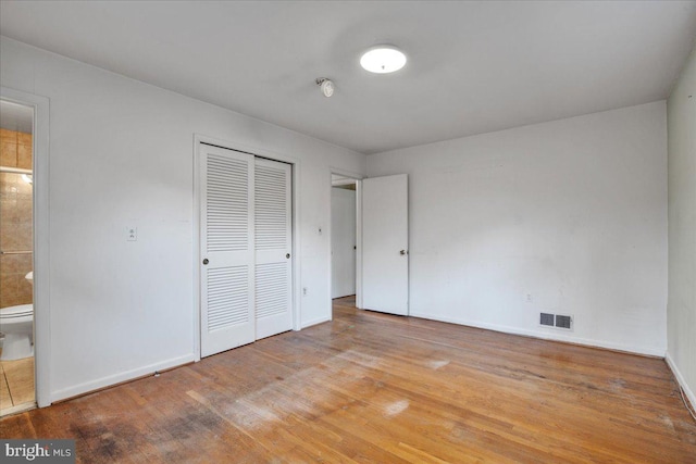 unfurnished bedroom featuring ensuite bath, a closet, and light hardwood / wood-style flooring