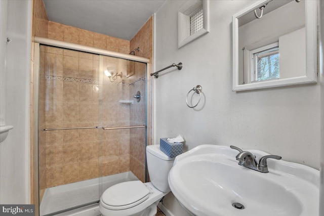 bathroom featuring toilet, a shower with door, and sink