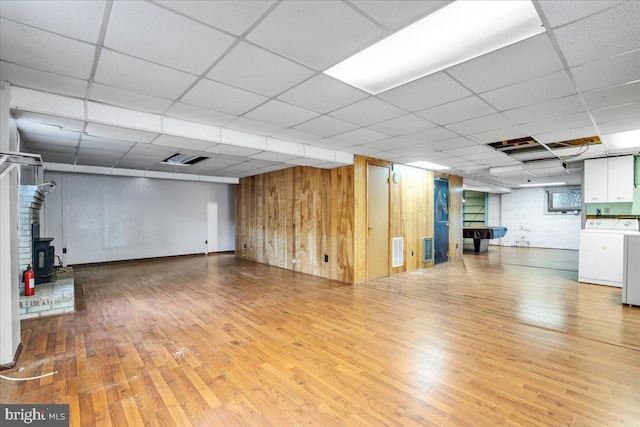 basement featuring washer / clothes dryer, a paneled ceiling, wood-type flooring, and a wood stove