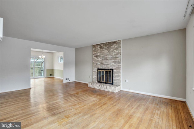 unfurnished living room with light hardwood / wood-style floors, a fireplace, and an inviting chandelier