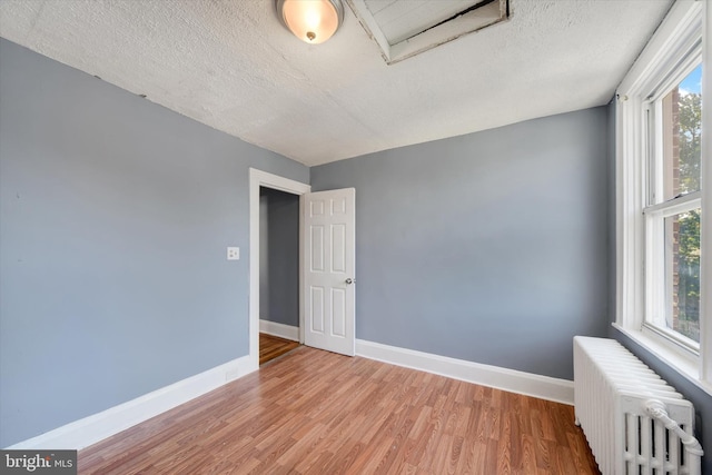 spare room featuring radiator heating unit, light hardwood / wood-style floors, and a textured ceiling