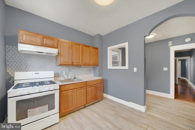 kitchen featuring light wood-type flooring, backsplash, gas range gas stove, a textured ceiling, and sink