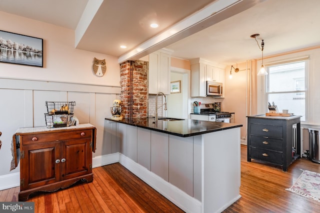 kitchen with kitchen peninsula, appliances with stainless steel finishes, sink, hardwood / wood-style floors, and white cabinetry