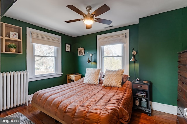 bedroom with radiator, ceiling fan, dark wood-type flooring, and multiple windows