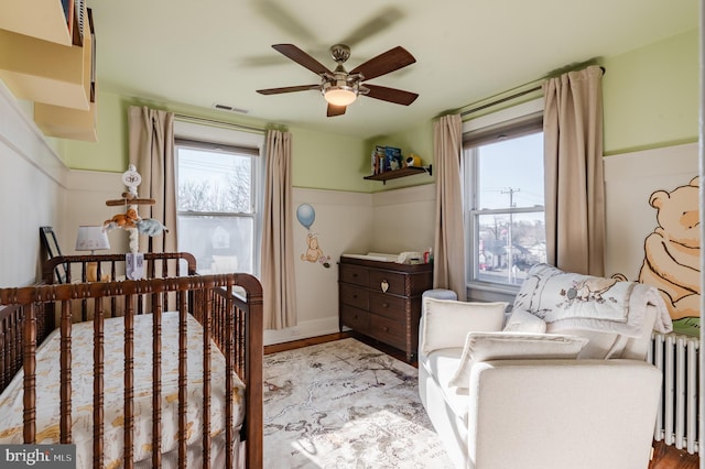 bedroom featuring ceiling fan, light wood-type flooring, a crib, and radiator