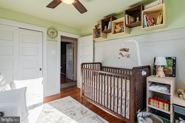 bedroom featuring ceiling fan, a closet, a crib, and hardwood / wood-style flooring