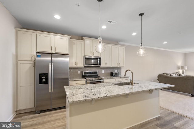 kitchen featuring sink, stainless steel appliances, decorative light fixtures, and a center island with sink