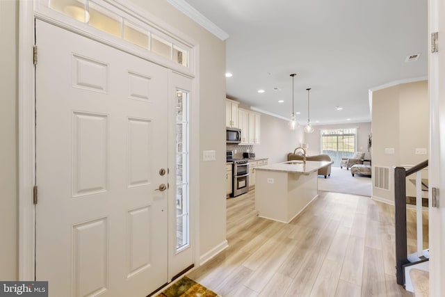 foyer with light wood-type flooring, crown molding, and sink