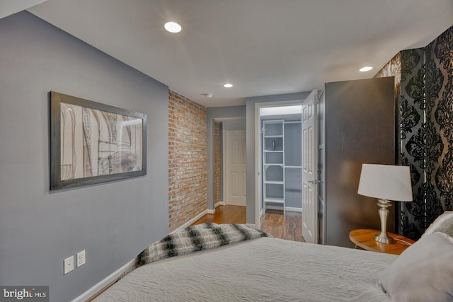 bedroom featuring a walk in closet, a closet, hardwood / wood-style floors, and brick wall