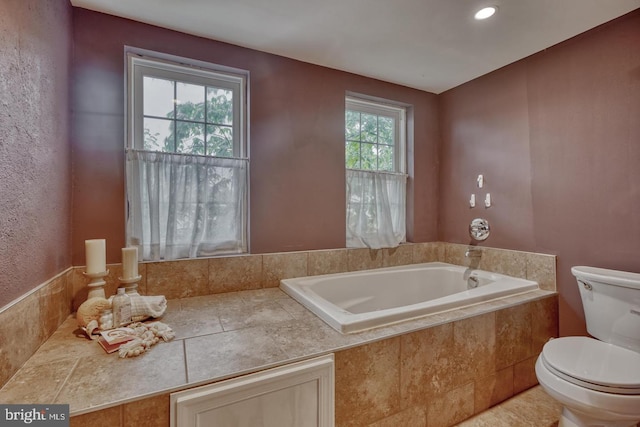 bathroom featuring tiled tub, a wealth of natural light, and toilet