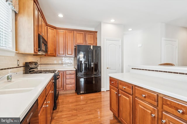 kitchen featuring light hardwood / wood-style floors, sink, decorative backsplash, and black appliances