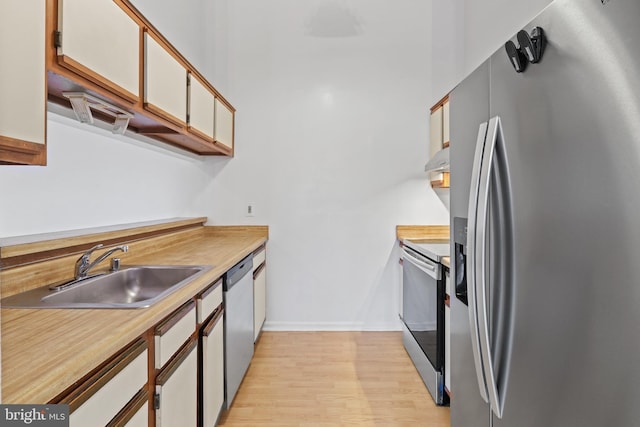 kitchen with white cabinets, appliances with stainless steel finishes, light hardwood / wood-style flooring, and sink