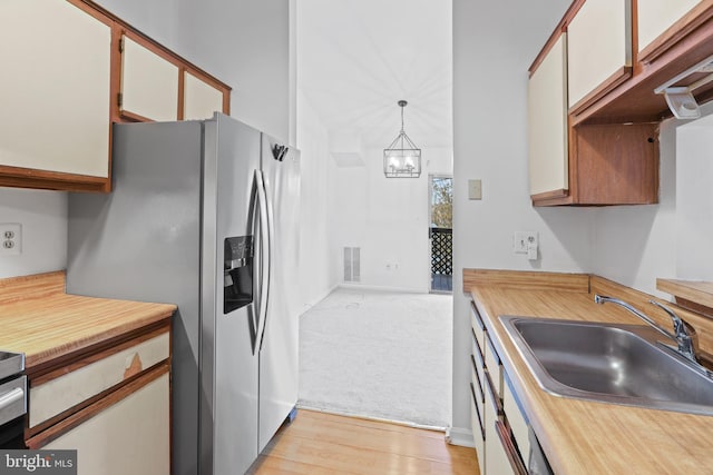 kitchen featuring white cabinetry, sink, stainless steel fridge with ice dispenser, pendant lighting, and light hardwood / wood-style floors