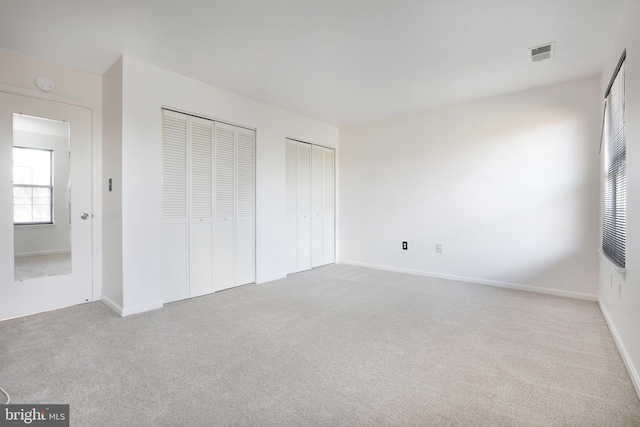 unfurnished bedroom featuring light carpet and multiple closets