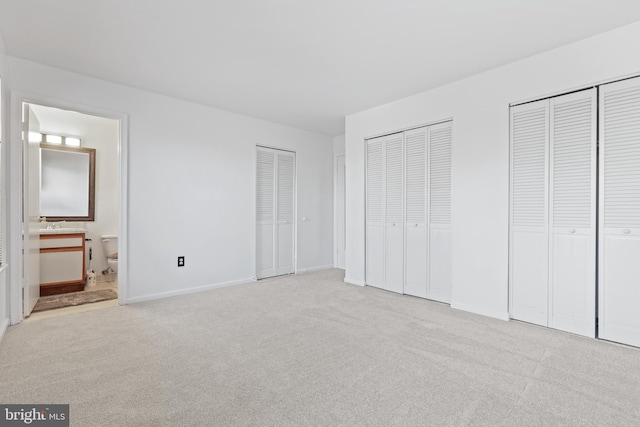 unfurnished bedroom with light colored carpet, connected bathroom, and two closets