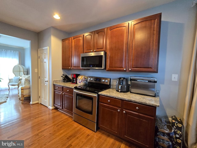 kitchen featuring light stone countertops, appliances with stainless steel finishes, and light wood-type flooring