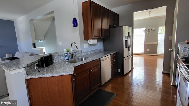 kitchen featuring light stone countertops, stainless steel appliances, sink, a notable chandelier, and hardwood / wood-style floors