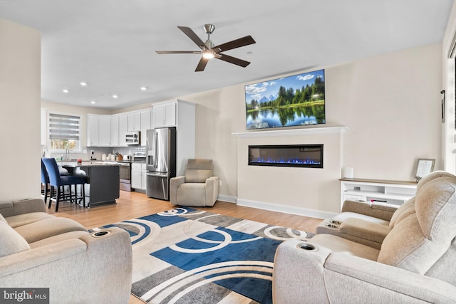 living room with light hardwood / wood-style flooring, ceiling fan, and sink