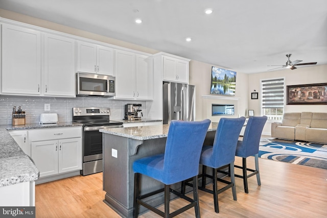 kitchen featuring light stone countertops, white cabinets, stainless steel appliances, and light hardwood / wood-style floors