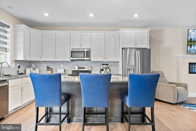 kitchen with light stone countertops, stainless steel appliances, a kitchen island, and white cabinetry