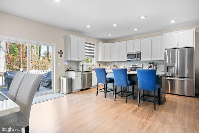 kitchen featuring white cabinetry, stainless steel appliances, a breakfast bar area, decorative backsplash, and light wood-type flooring