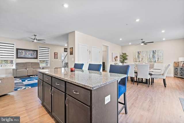 kitchen with light hardwood / wood-style flooring, light stone countertops, dark brown cabinets, a kitchen island, and a kitchen bar