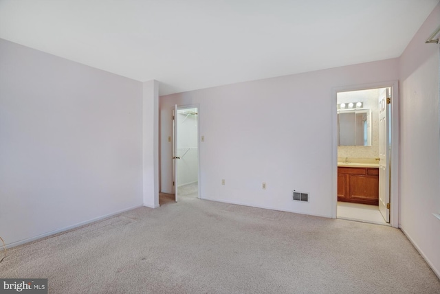 unfurnished bedroom featuring a closet, ensuite bath, a spacious closet, and light colored carpet