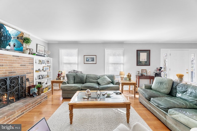 living room with a brick fireplace, ornamental molding, and light wood-type flooring