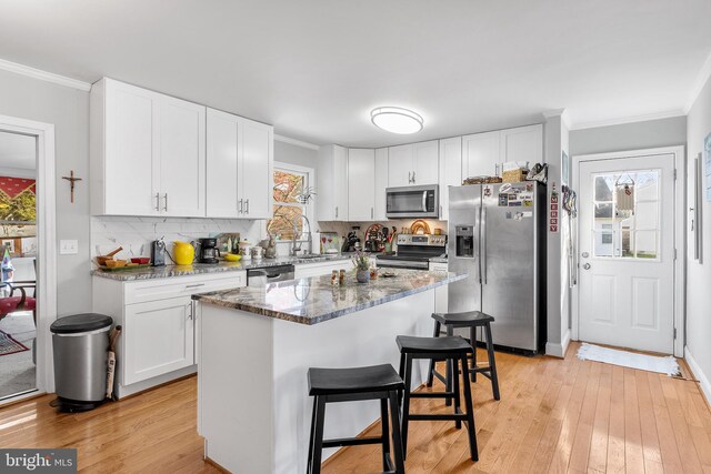 kitchen with white cabinets, stainless steel appliances, a wealth of natural light, and light hardwood / wood-style flooring