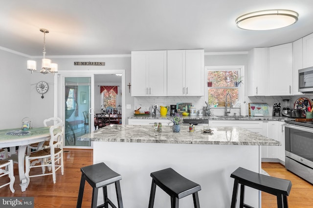 kitchen with light stone countertops, a center island, stainless steel appliances, light hardwood / wood-style flooring, and white cabinets