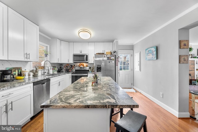 kitchen with white cabinets, stainless steel appliances, a kitchen island, and stone countertops