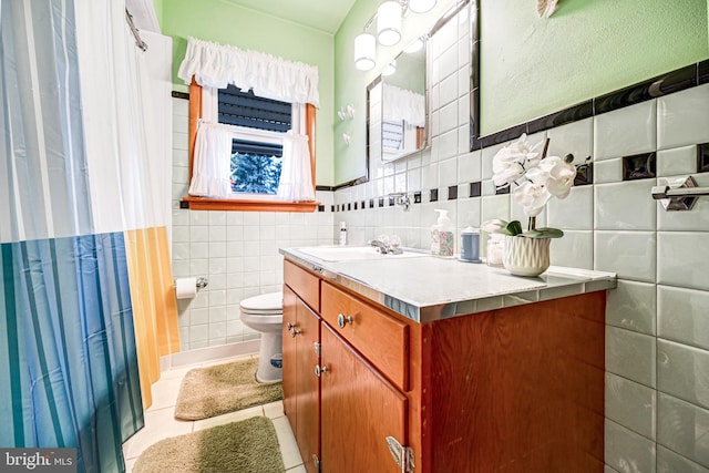 bathroom featuring toilet, vanity, tile patterned floors, and tile walls