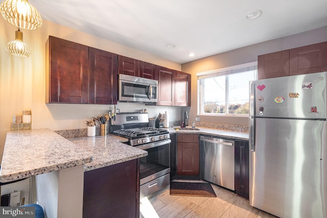 kitchen with kitchen peninsula, light stone counters, stainless steel appliances, sink, and pendant lighting