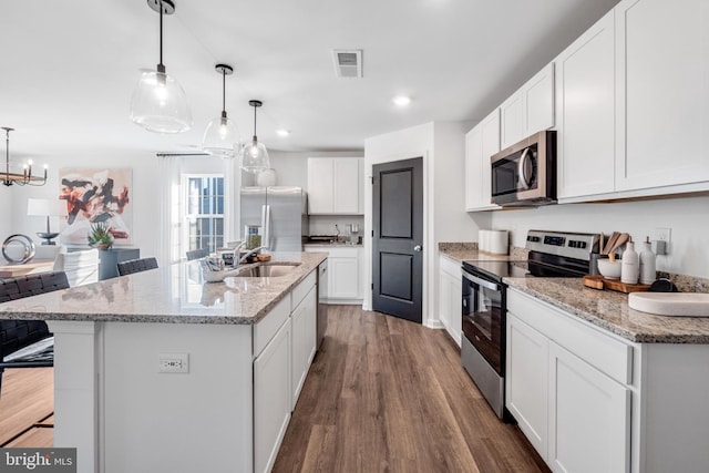 kitchen with hanging light fixtures, stainless steel appliances, white cabinetry, and a kitchen island with sink