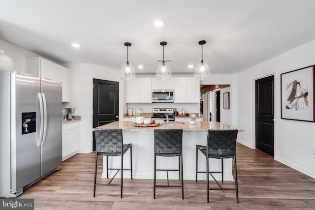 kitchen with a kitchen island with sink, white cabinets, hanging light fixtures, and appliances with stainless steel finishes