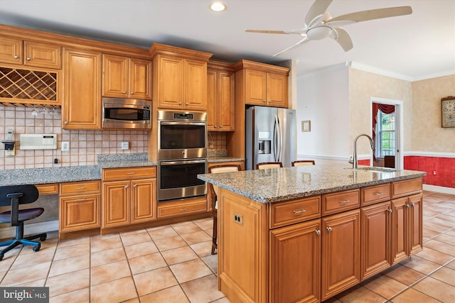 kitchen with a center island with sink, crown molding, sink, light stone countertops, and appliances with stainless steel finishes