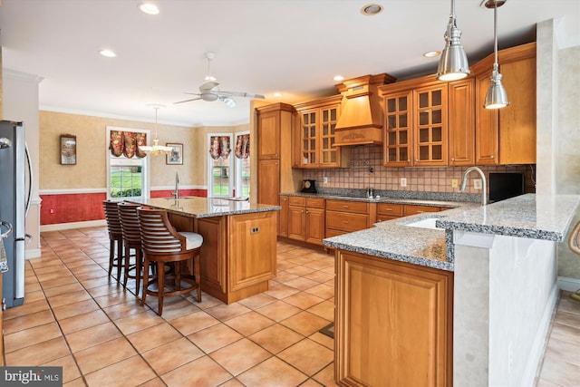 kitchen featuring kitchen peninsula, light stone counters, custom exhaust hood, a breakfast bar, and crown molding