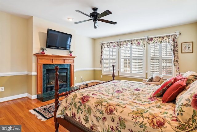 bedroom featuring ceiling fan, light hardwood / wood-style flooring, and a premium fireplace