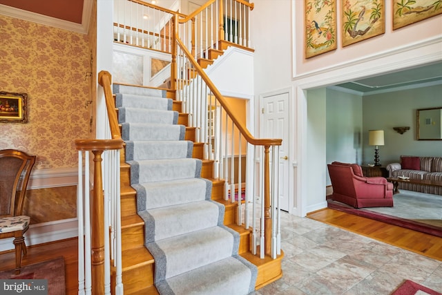 stairs featuring hardwood / wood-style floors, ornamental molding, and a towering ceiling