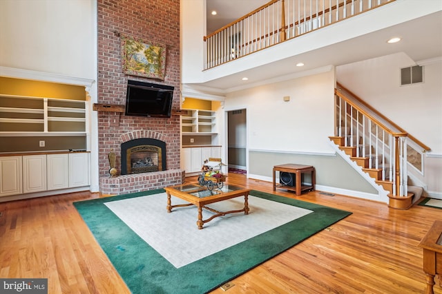 living room featuring built in features, crown molding, hardwood / wood-style floors, a towering ceiling, and a fireplace