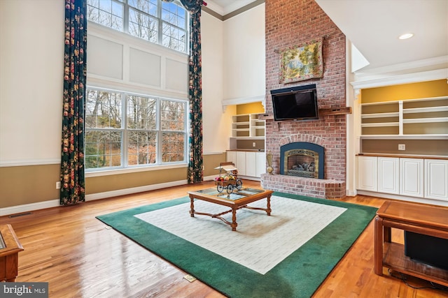 living room featuring hardwood / wood-style floors, a healthy amount of sunlight, ornamental molding, and a brick fireplace