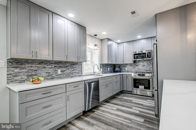 kitchen featuring gray cabinetry, sink, appliances with stainless steel finishes, decorative light fixtures, and wood-type flooring