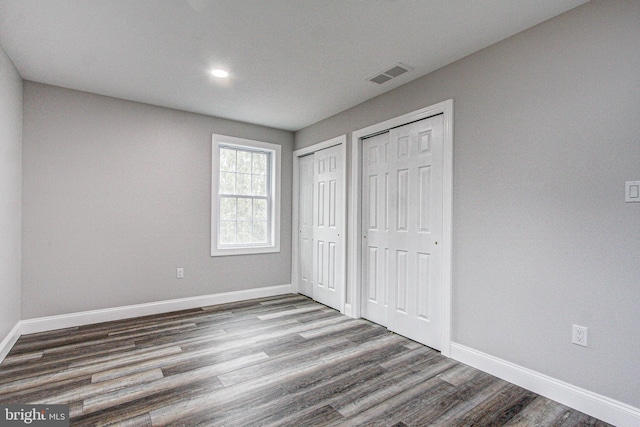 unfurnished bedroom featuring wood-type flooring and two closets