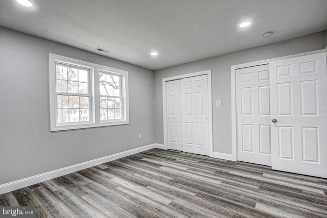 unfurnished bedroom with hardwood / wood-style floors and multiple closets